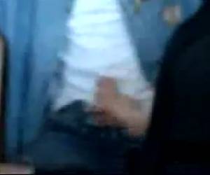 Op de achterste rij van de klas zitten een meisje en een jongen naast elkaar in de schoolbank. Het meisje maakt de rits van de jongen open en begint hem af te trekken.